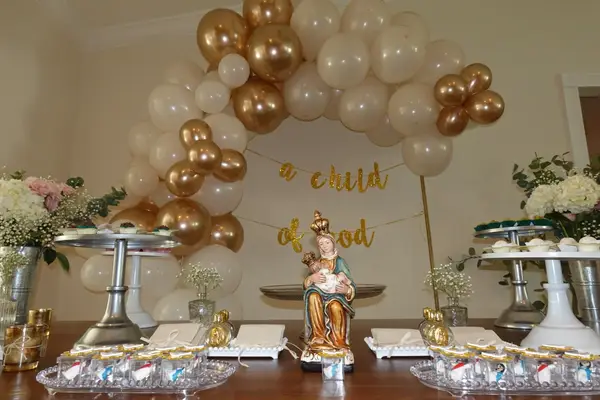Gold and white baptism dessert table with organic balloon arch and religious decor for elegant christening celebration in South Florida